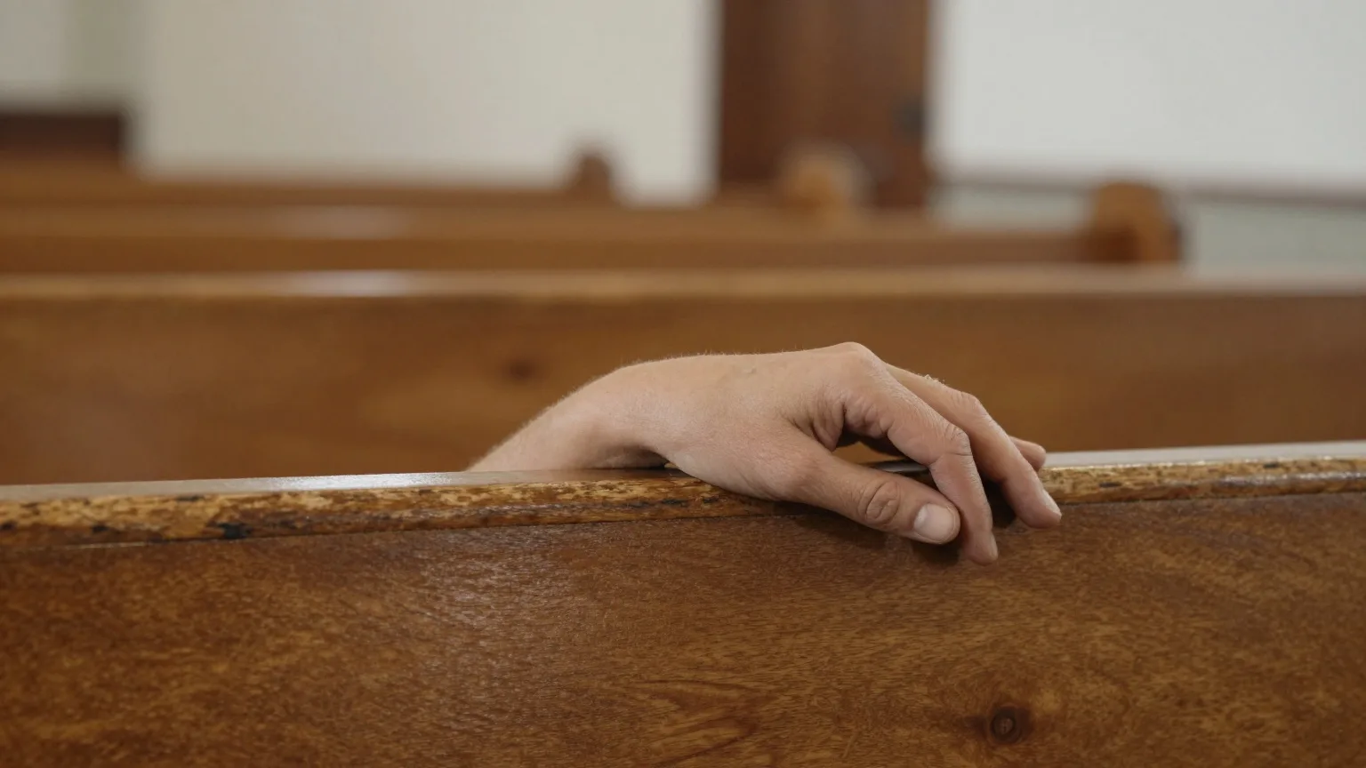 Gefaltete Hände auf der Lehne einer abgenutzten Kirchenbank
