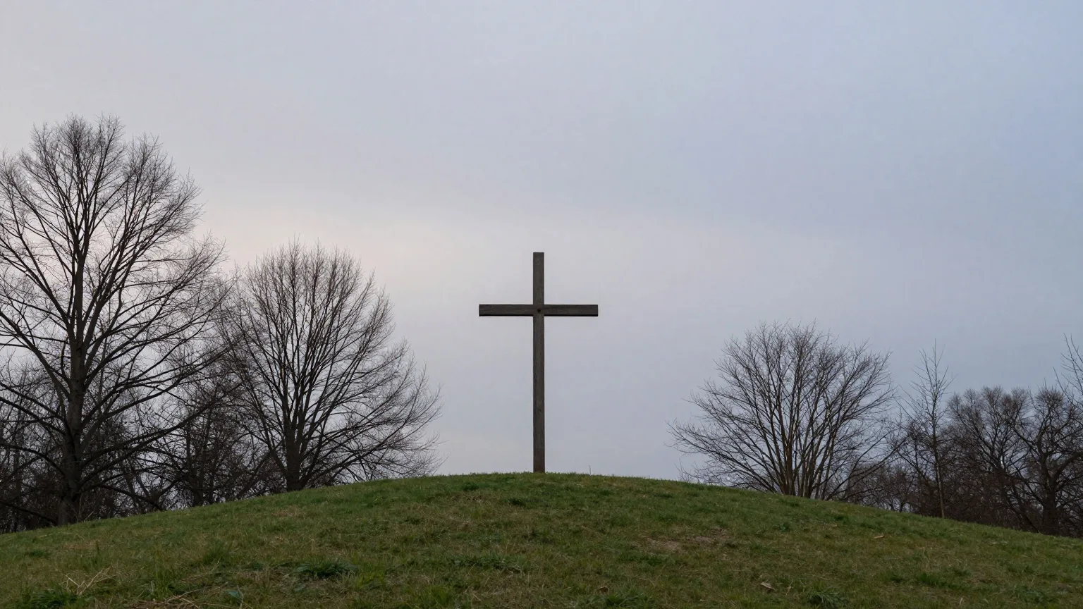 Schlichtes Holzkreuz auf einem Hügel unter bewölktem Abendhimmel
