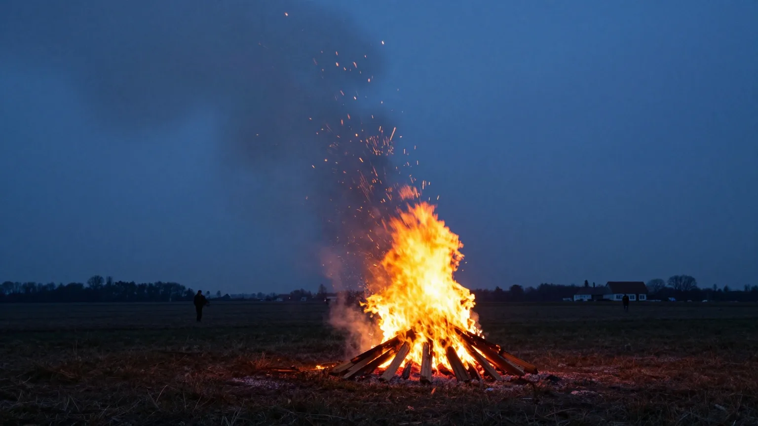 Osterfeuer auf einem Feld in der Abenddämmerung, Menschen in der Ferne