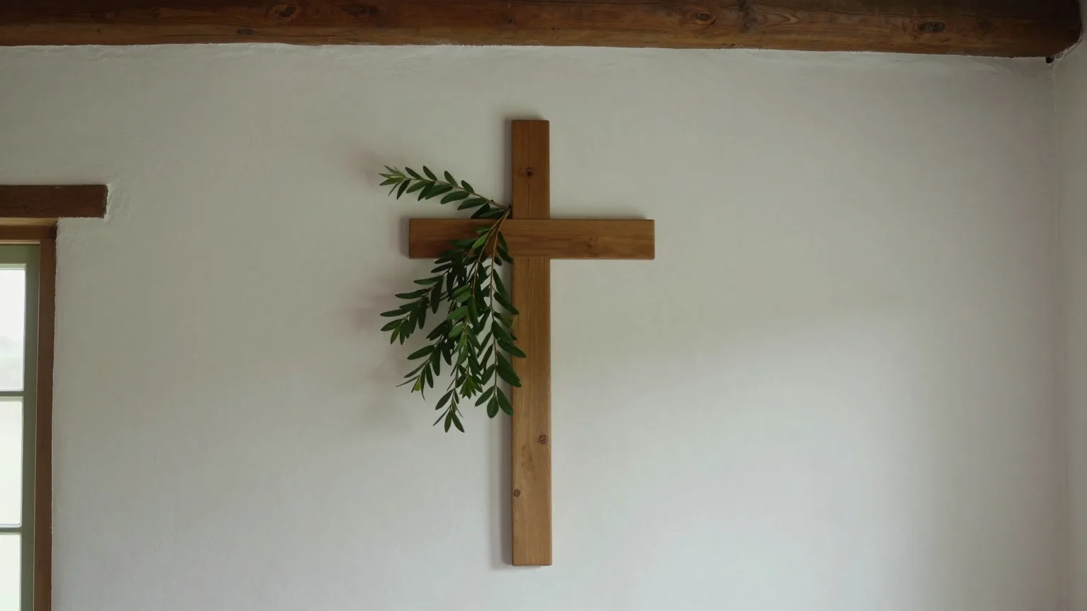 Gesegneter Buchsbaumzweig hinter einem schlichten Holzkreuz an der weiß gekalkten Wand einer Bauernstube