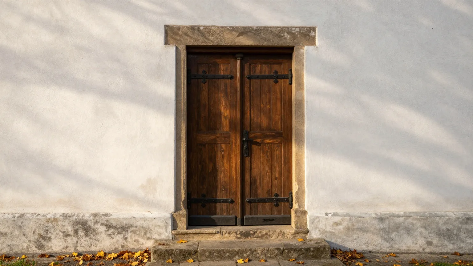 Schwere alte Holztür mit Eisenbeschlägen in einer weiß gekalkten Kirchenmauer im Herbstlicht