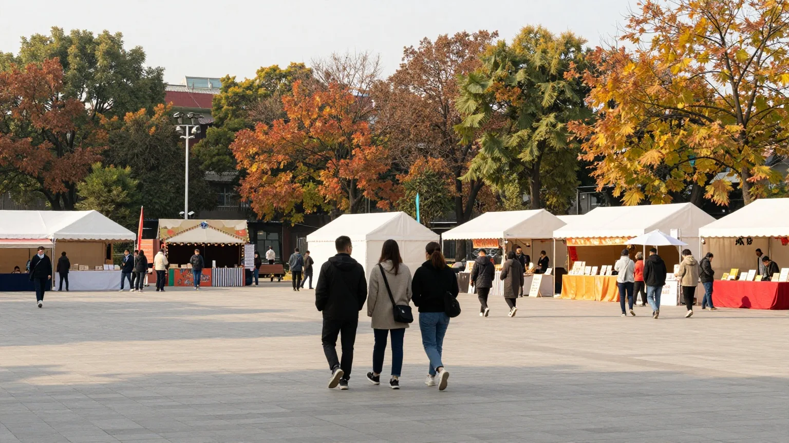Menschen von hinten zwischen weißen Festzelten auf einem Platz an einem sonnigen Herbsttag