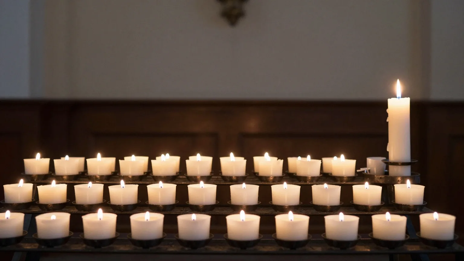 Viele kleine weiße Kerzen brennen auf einem Kerzenständer in einer dunklen Kirche