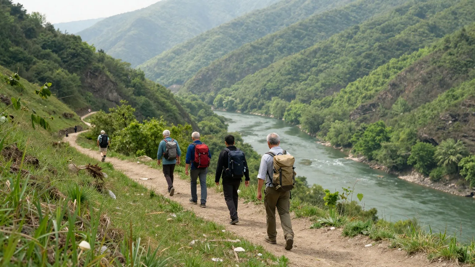 Gruppe von Männern von hinten mit Rucksäcken auf einem Höhenweg über einem grünen Flusstal