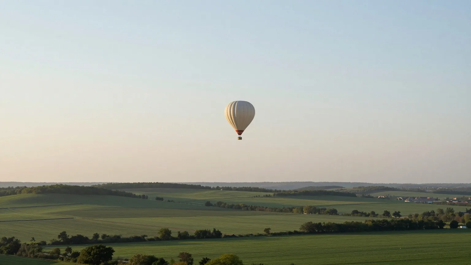 Heißluftballon in der Ferne über einer grünen Hügellandschaft im Mai