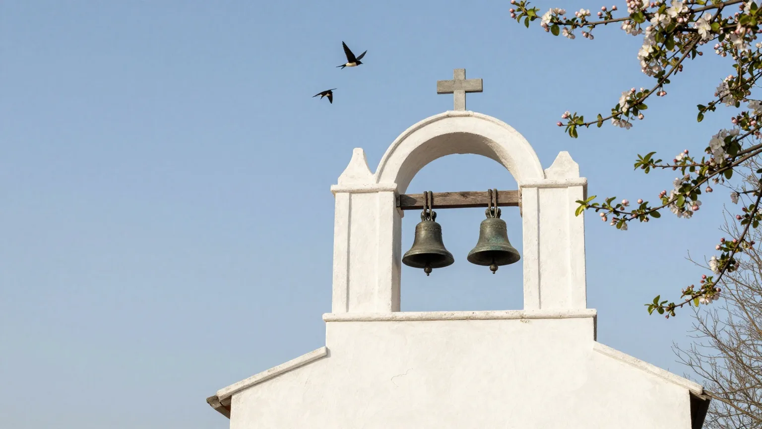 Offener Glockenstuhl mit Bronzeglocken neben einer weißen Kirche vor klarem Aprilhimmel