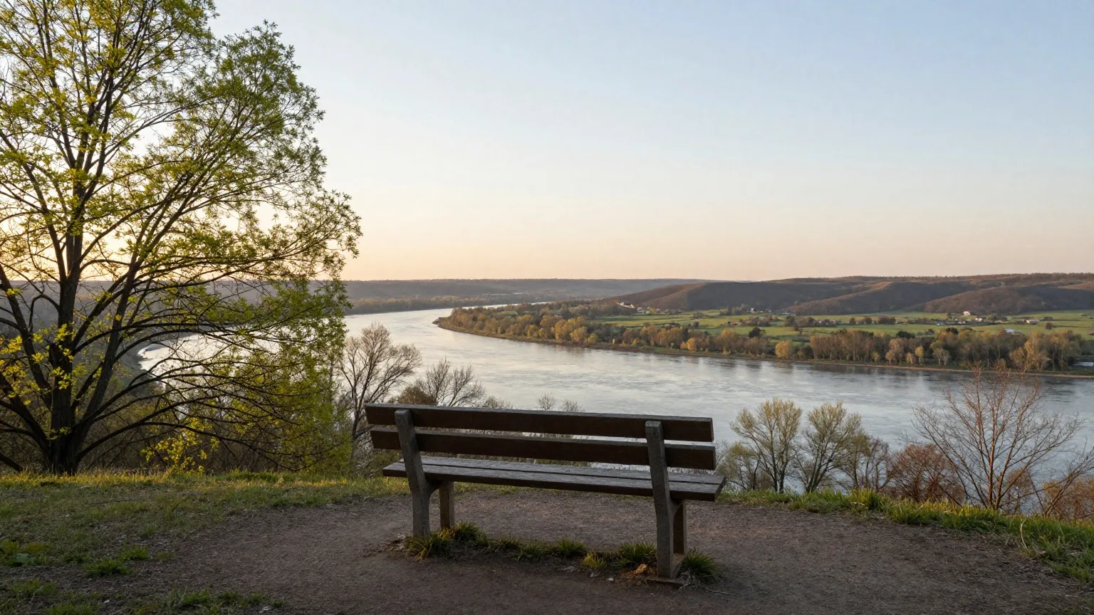 Holzbank an einem Aussichtspunkt über einem Flusstal im langen Abendlicht Ende März