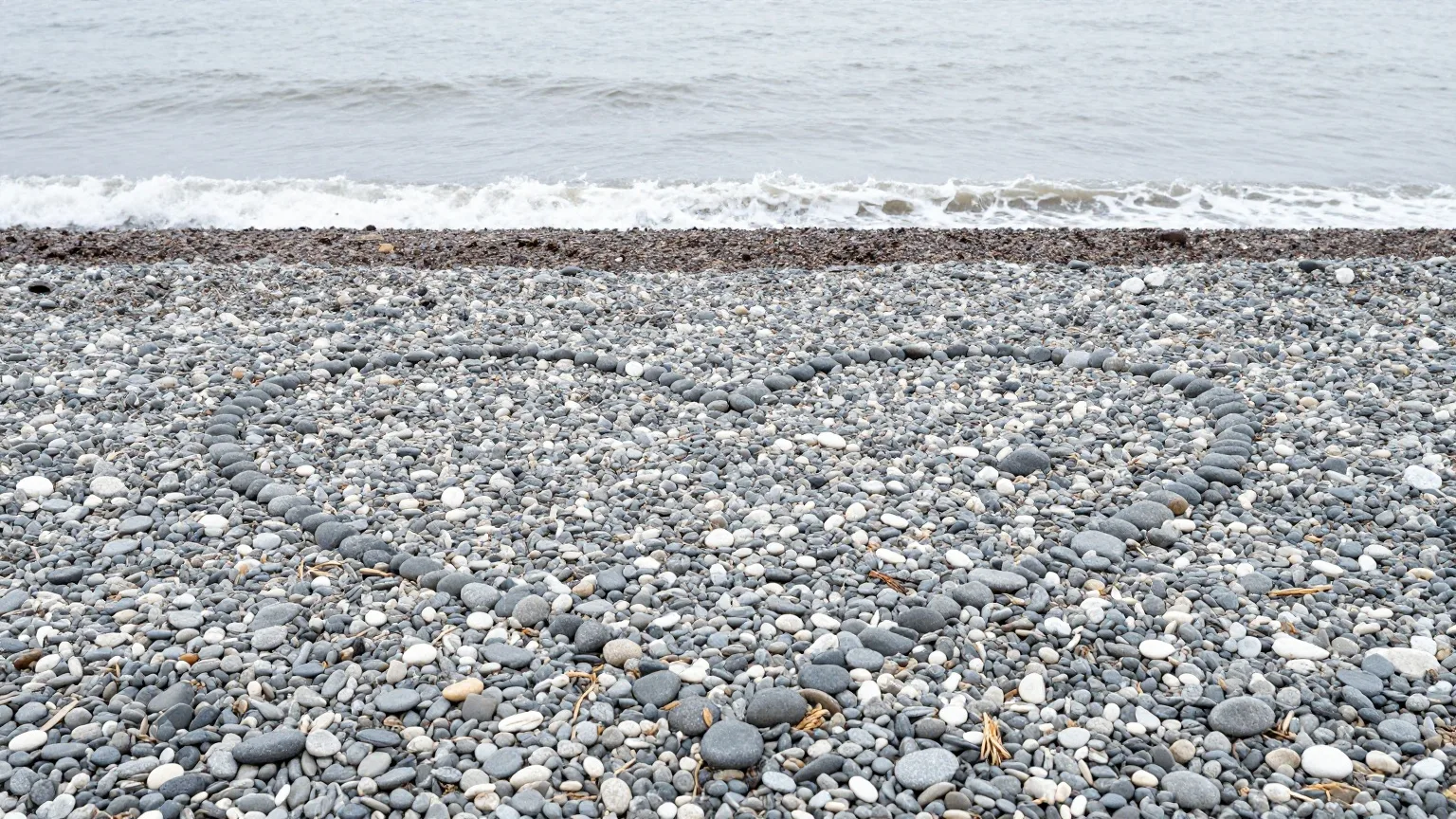 Aus Kieselsteinen gelegtes Herz an einem winterlichen Kiesstrand