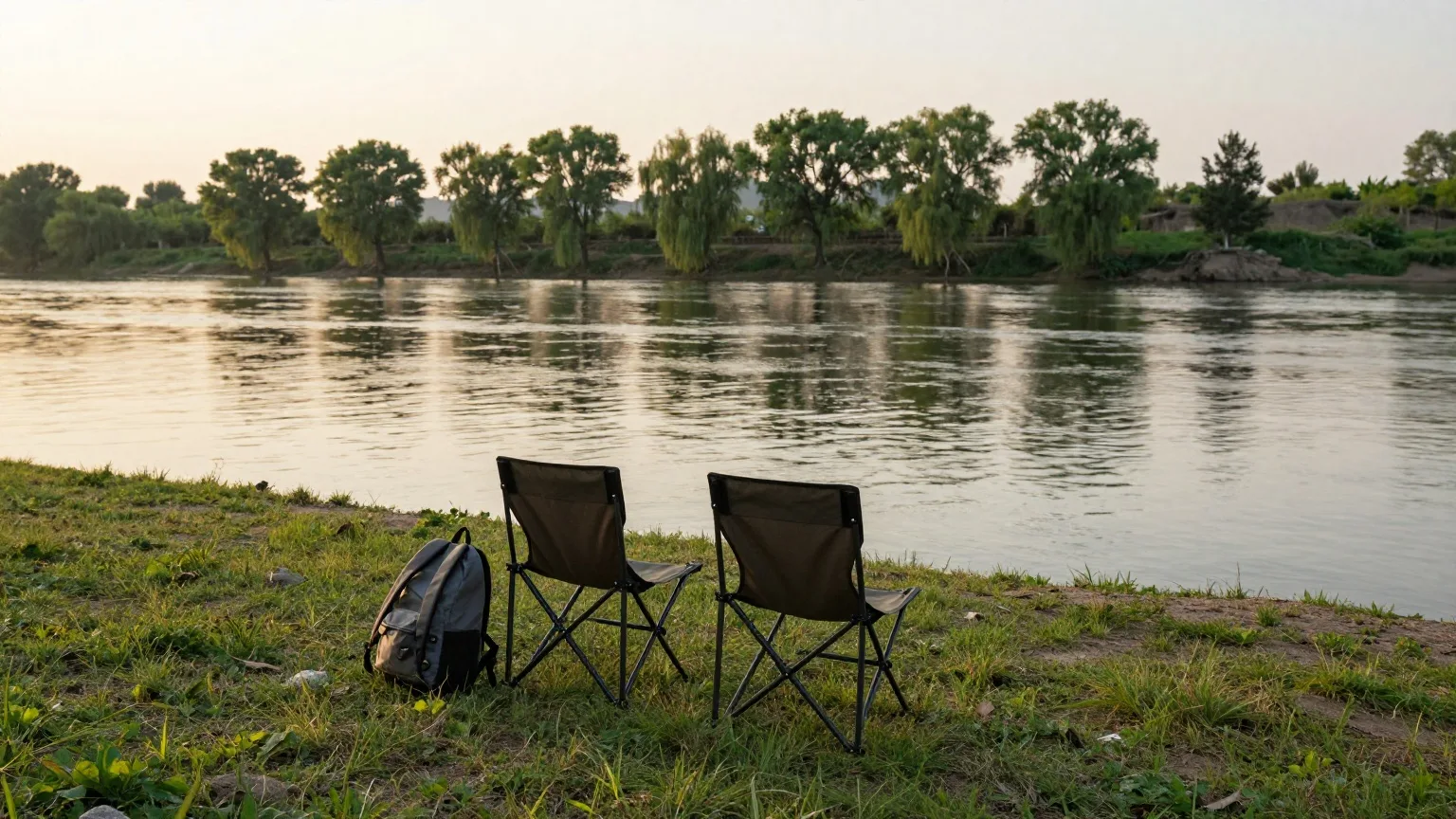 Zwei leere Campingstühle am Ufer eines Flusses im späten Abendlicht Ende Mai