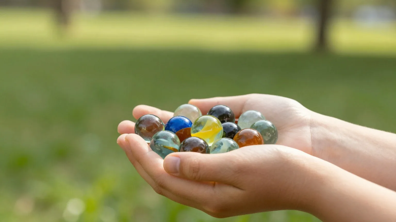 Kinderhände halten bunte Glasmurmeln im warmen Spätsommerlicht