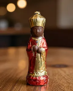 Schokoladennikolaus in roter und goldener Folie ohne Gesicht in Großaufnahme vor warmen Lichtern