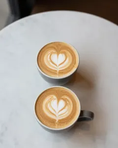 Zwei Cappuccino mit Milchschaum-Herz auf einem hellen Marmortisch