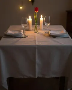 Gedeckter Tisch für zwei mit brennenden Kerzen und einer roten Tulpe