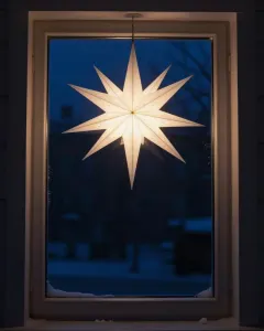 Leuchtender weißer Herrnhuter Stern in einem dunklen, verschneiten Fenster
