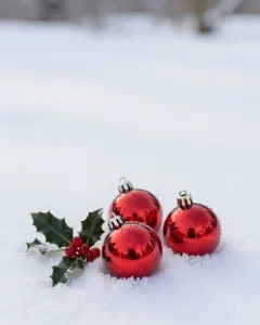 Drei rote Christbaumkugeln und ein Stechpalmenzweig im frischen Pulverschnee