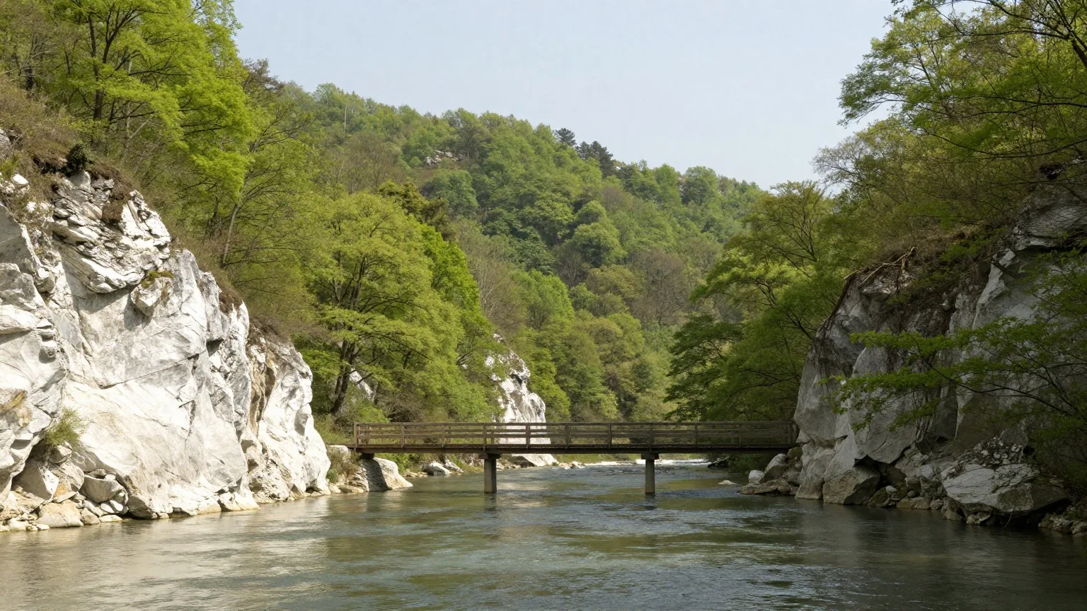 Kalkfelsen und hölzerner Steg über einem stillen Flusstal Ende Mai