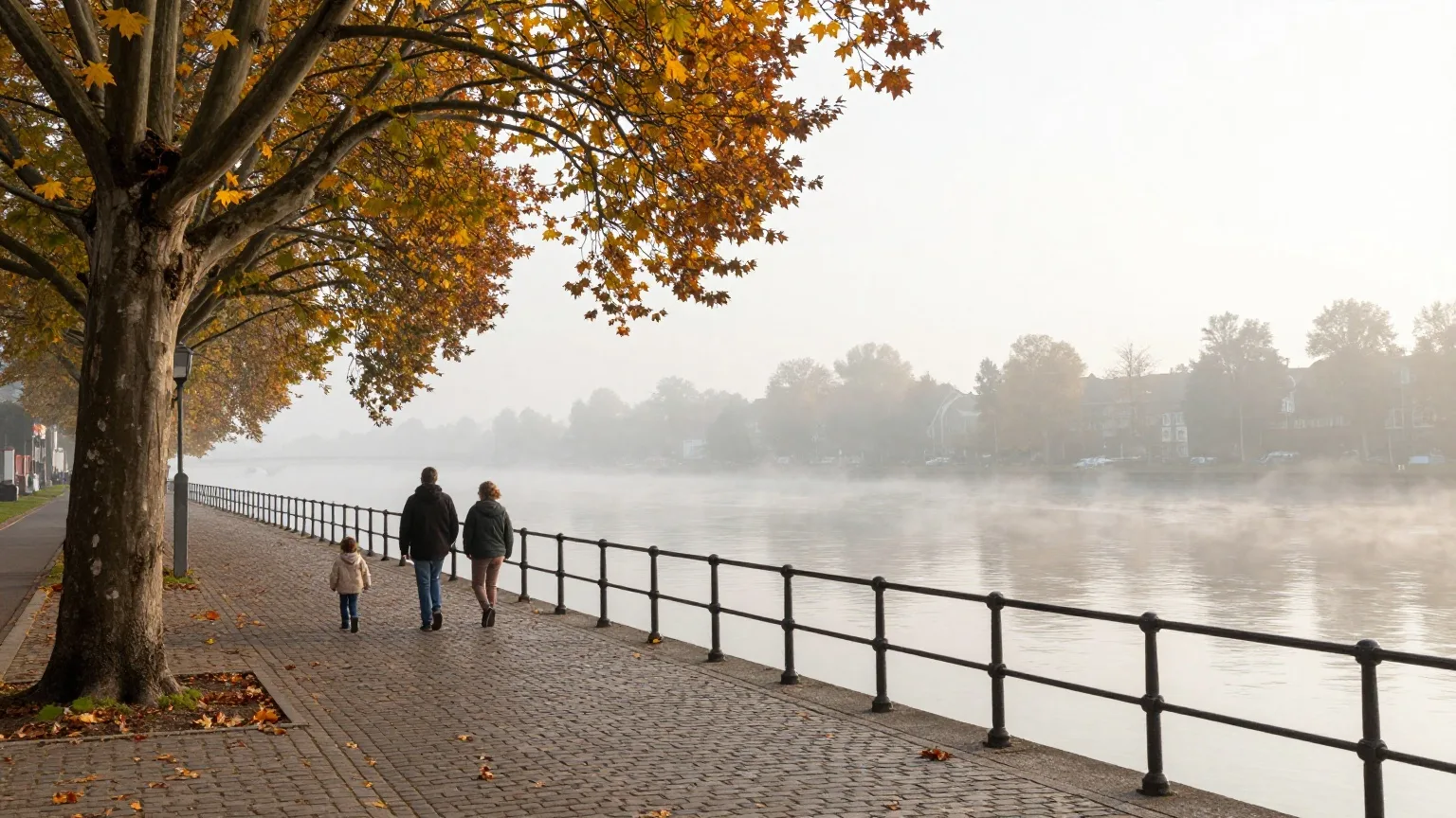 Uferpromenade an einem breiten Fluss mit Herbstlaub, eine Familie geht von hinten gesehen am Geländer entlang