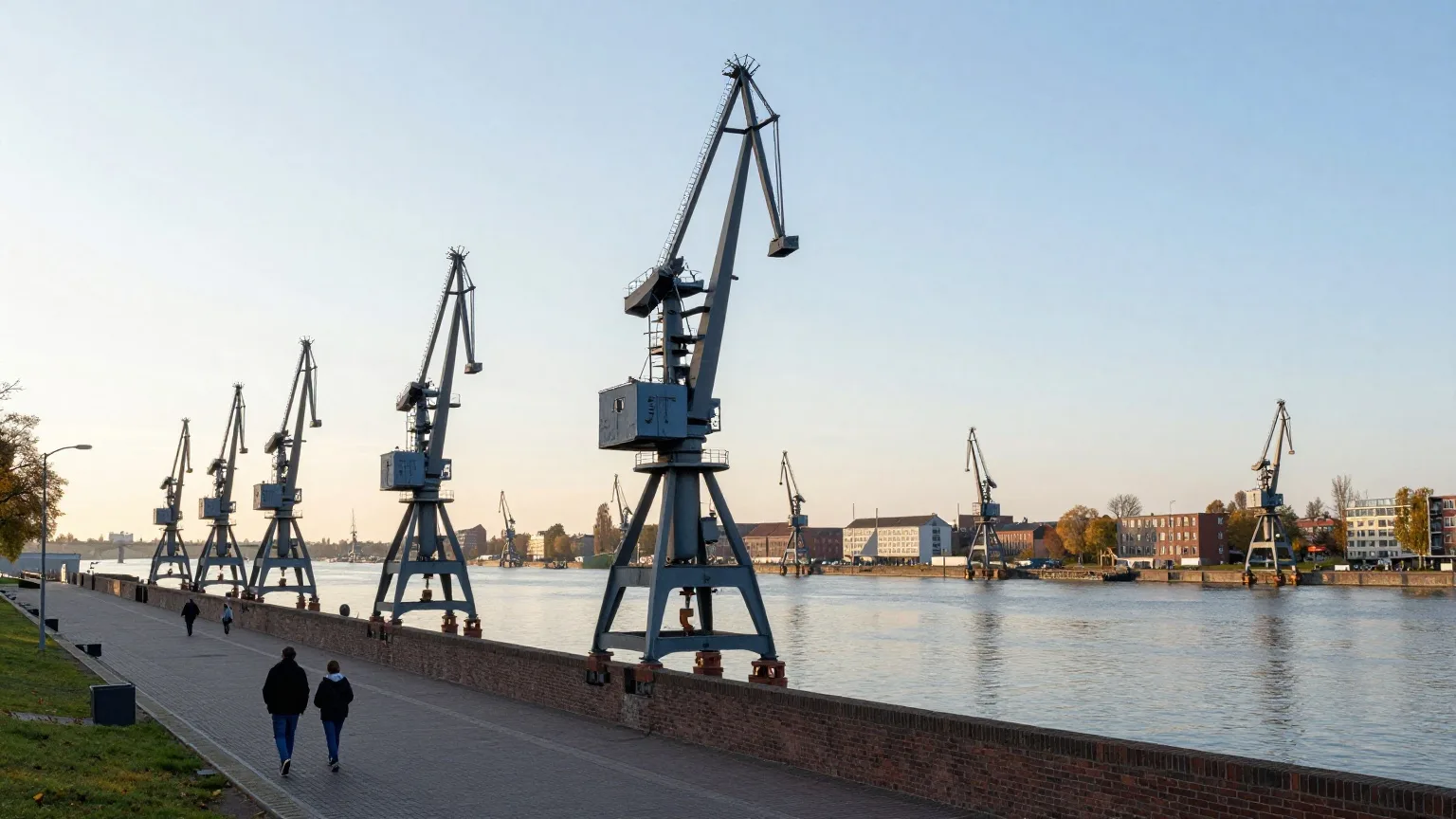 Historische Hafenkräne an einer Kaimauer im Abendlicht eines Oktobertags, eine Familie geht von hinten auf der Uferpromenade