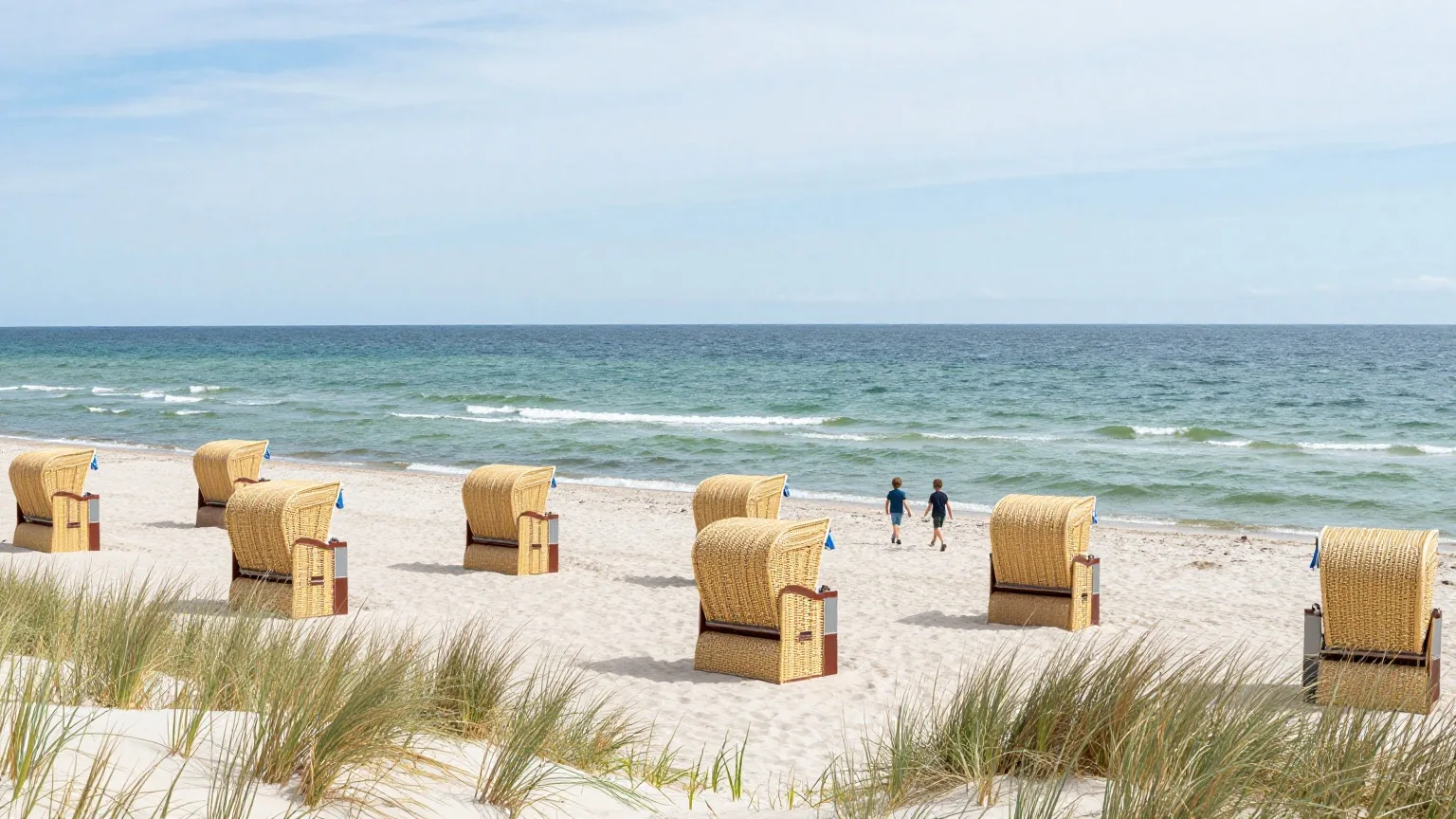 Kinder laufen von hinten gesehen über einen weißen Ostseestrand mit Strandkörben zum Wasser