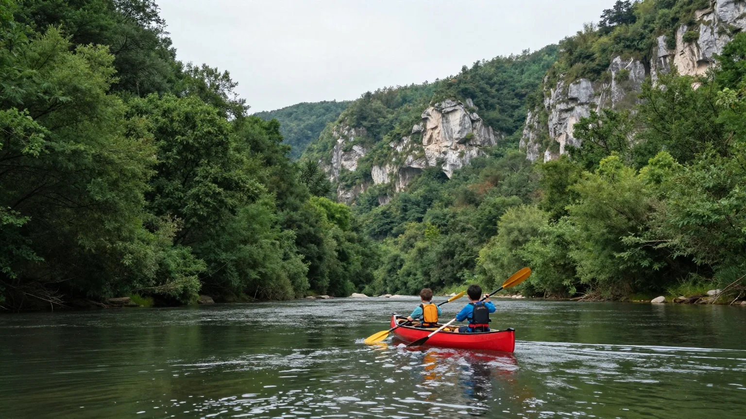 Zwei Kinder im Kanu von hinten auf einem Fluss in einem bewaldeten Tal im Sommer