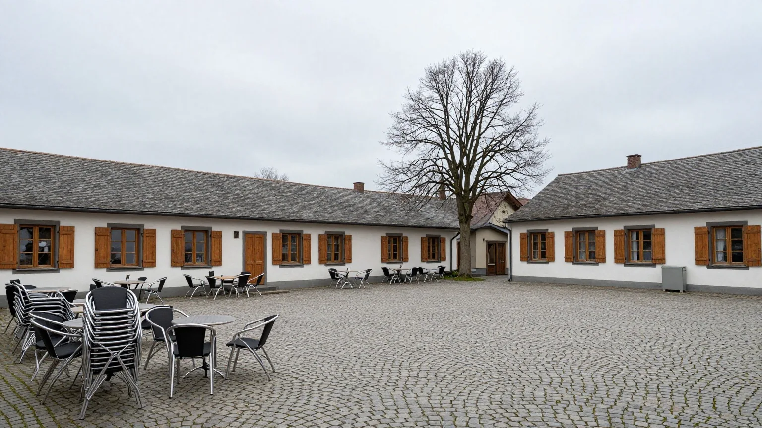 Menschenleerer Marktplatz mit Kopfsteinpflaster an einem grauen Vormittag, die Stühle eines Cafés sind gestapelt