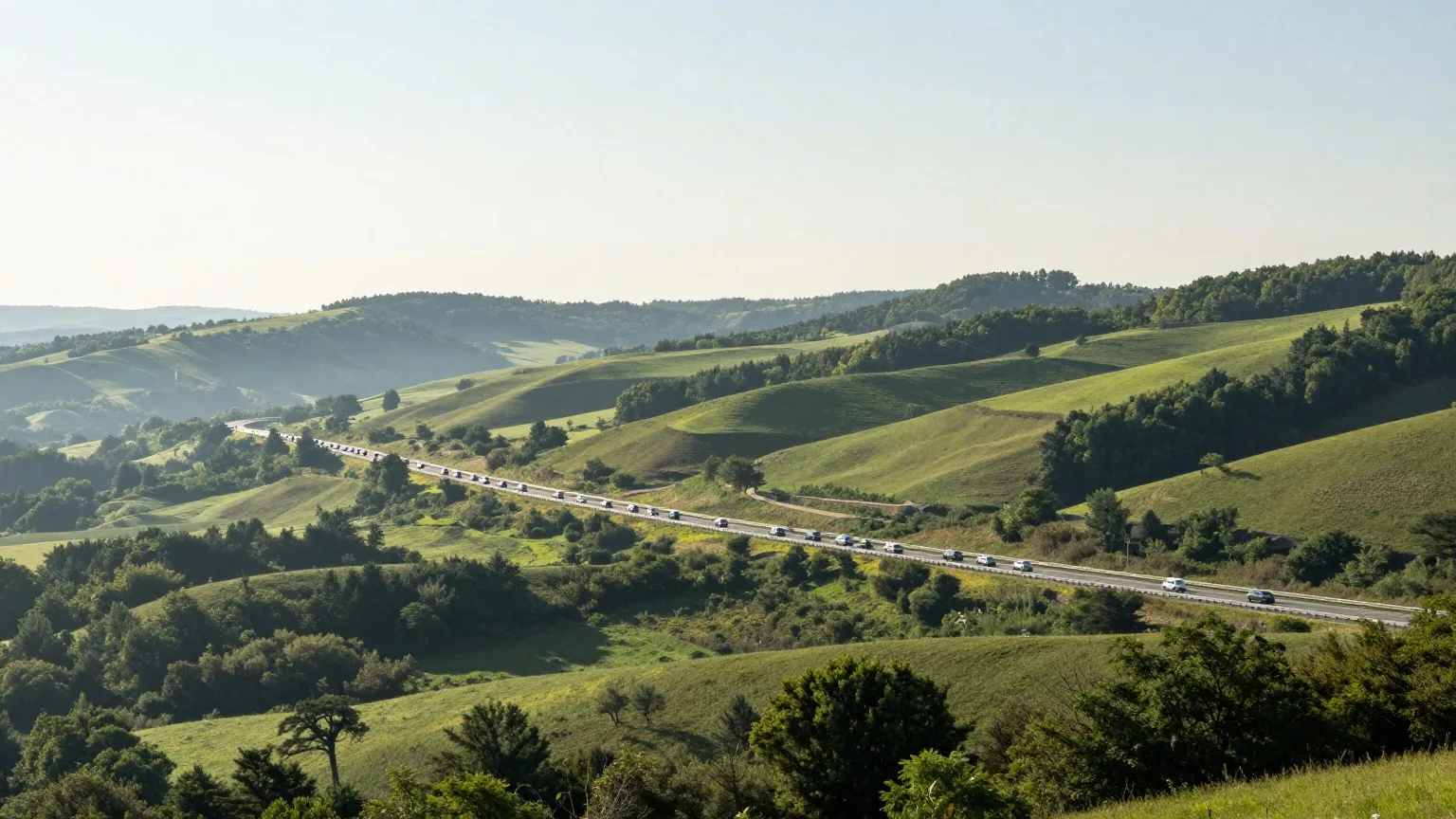 Lange Autokolonne auf einer Autobahn zwischen grünen Hügeln, aus großer Entfernung fotografiert