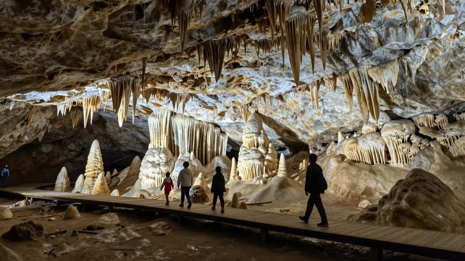 Familie geht von hinten gesehen über einen beleuchteten Holzsteg durch eine Tropfsteinhöhle